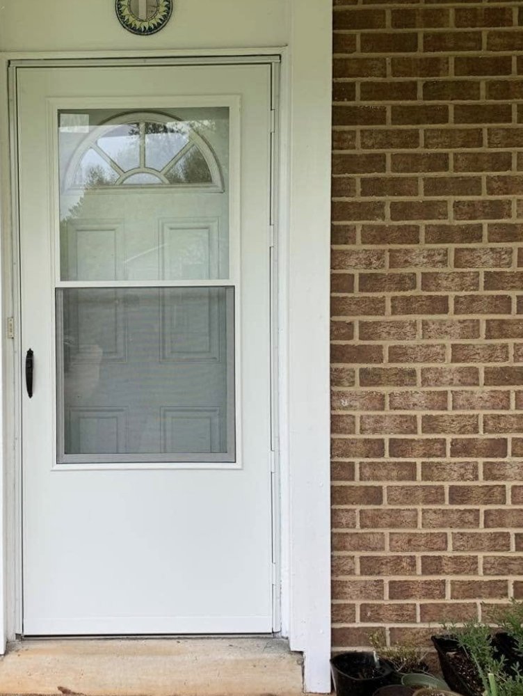White storm door with a screen panel installed on a brick front entry